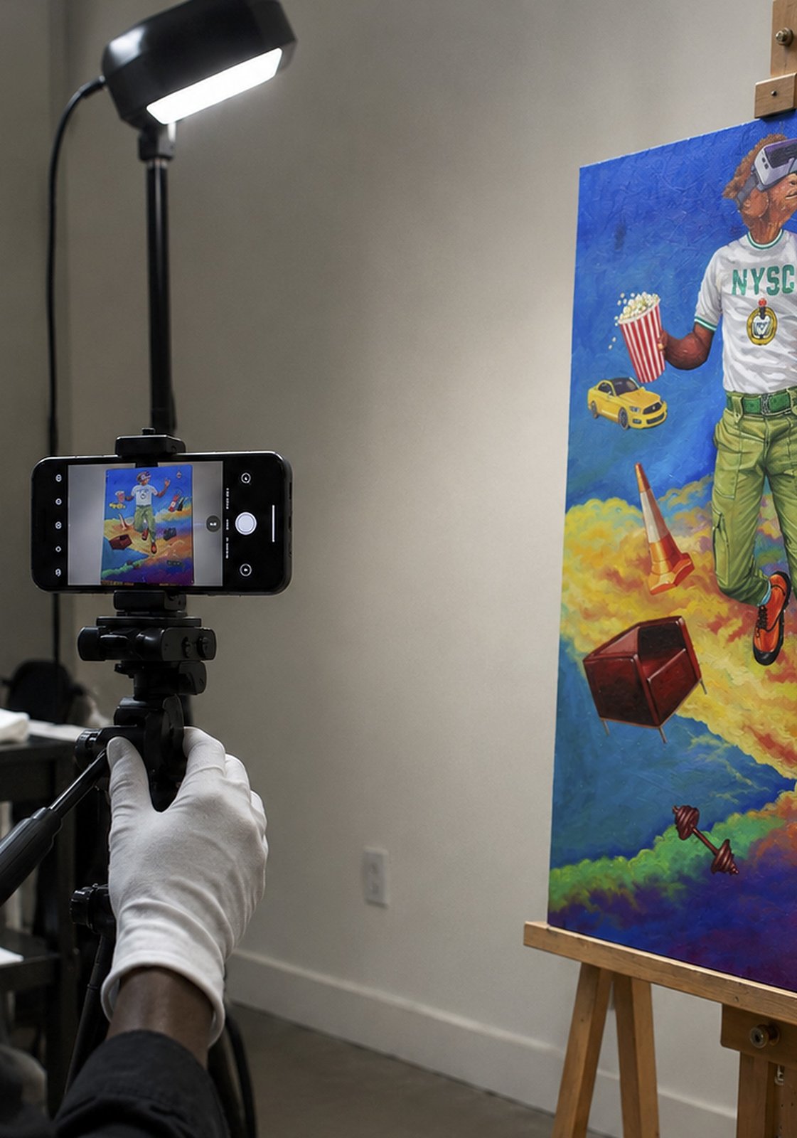 A gloved hand steadies a phone on a tripod in front of Virtual Reality on an easel, lit by a single lamp.